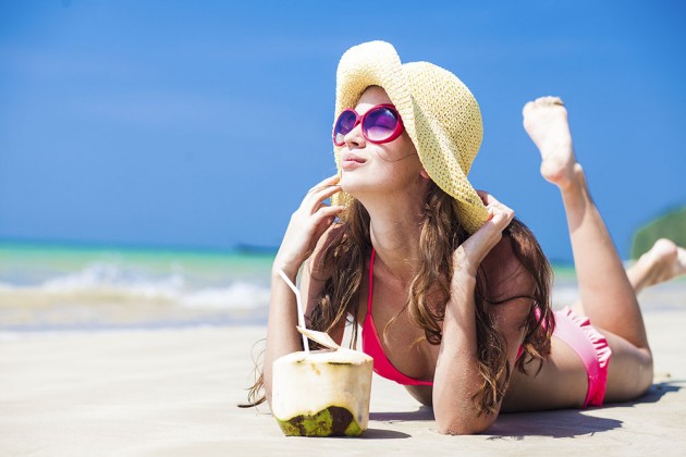 Young farang woman smiling lying in straw hat in sunglasses with coconut on beach.Thailand-Property.com