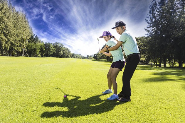 Young female golf player at Driving Range with a Golf Pro, she presumably does exercise